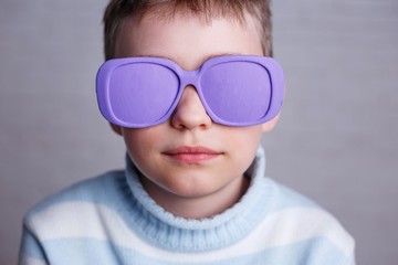 Close up portrait of cute boy in violet sunglasses with opaque lenses