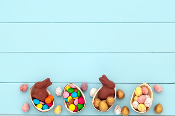 Easter composition with chocolate rabbits, chocolate eggs and candies on a turquoise wooden background (copy space)