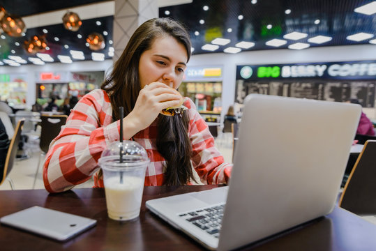 woman eat burger in cafe and watch laptop