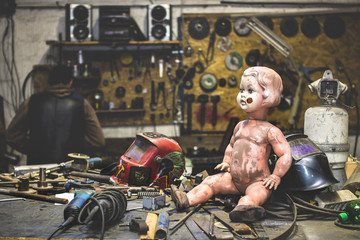 Dirty plastic baby doll posing inside of a metal shop