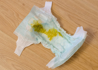 Closeup of yellow dirty stinky diaper of new born baby lying on the wooden floor