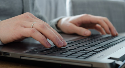 Closeup of young man hands with marriage ring typing on keyboard