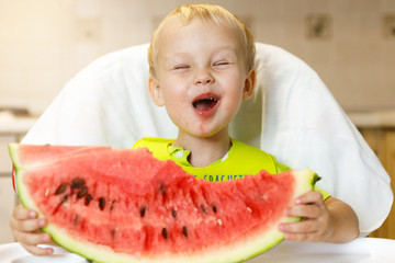 Happy baby eating a slice of a sweet delicious watermelon. Kid biting from a piece of watermelon and getting pleasure