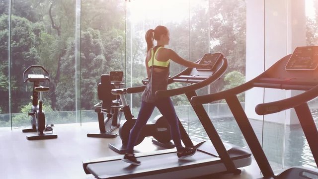 Cute Asian girl on treadmill at gym. Panoramic window, healthy fitness lifestyle concept
