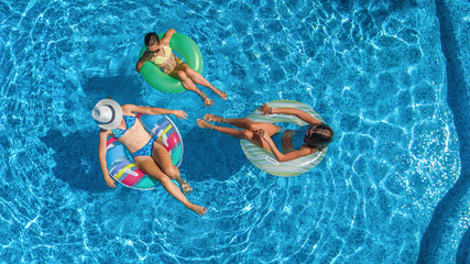 Aerial top view of family in swimming pool from above, happy mother and kids swim on inflatable ring donuts and have fun in water on family vacation, tropical holidays on resort
