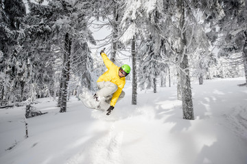 Man riding extremely a snowboard in the snowy forest jumping over the hump