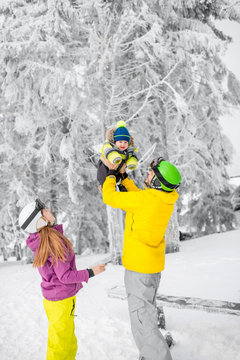 Happy family playing with baby boy standing in winter spots clothes outdoors during the winter vacations