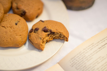 Table with chocolate chips cookies, book, cup of coofee, camera and hat