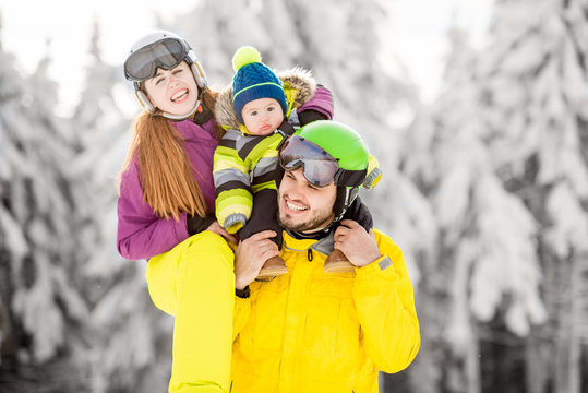 Portrait of a happy family playing with baby boy during the winter vacations on the beautiful mountains with snow-covered forest on the background