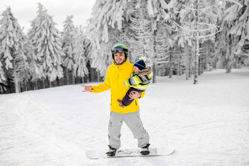 Man in colorful sports clothes riding the snowboard on the snowy mountains with beautiful trees on...