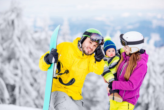 Portrait of a happy family with baby boy in winter sports clothes standing with snowboard during the winter vacations