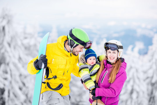 Portrait of a happy family with baby boy in winter sports clothes standing with snowboard during the winter vacations