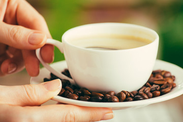 Young wooman hands with cup of coffee on green nature blurred background with bokeh