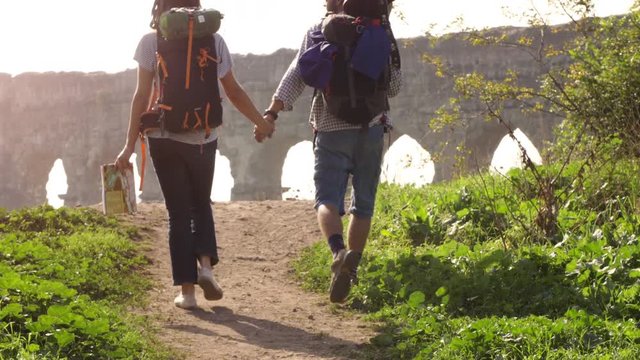 Young lovely couple backpackers tourists walking holding hands toward roman aqueduct arches in parco degli acquedotti park ruins in rome on romantic misty sunrise with guitar and sleeping bag slow