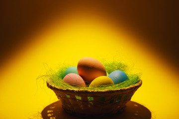 Colorful pastel monophonic traditional painted Easter eggs in basket with green grass on dark yellow background with black shadows, silhouette, light. Copy space for advertisement. With place for text