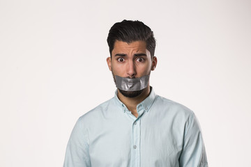 Portrait of a young man with tape on mouth over white background