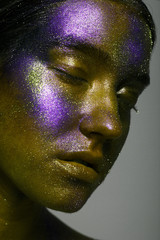 Creative make-up and beauty theme: beautiful girl model with cosmic make-up on face and body green and blue skin color on dark background in studio