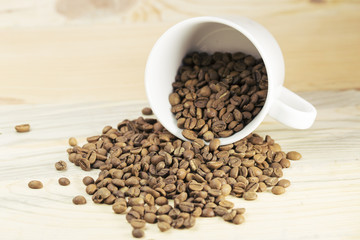 White cup full of coffee beans on Roasted Coffee Beans and wood background, top view