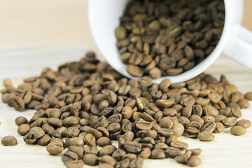 White cup full of coffee beans on Roasted Coffee Beans and wood background, top view