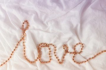 Beads in the shape of a word Love on a white fabric background