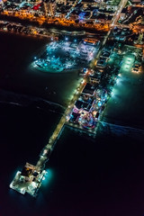 Aerial view of the Santa Monica shoreline, amusment park and pier at night with young woman holding out a smartphone in her hand