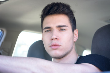 Serious young man or teenager driving car and looking at camera