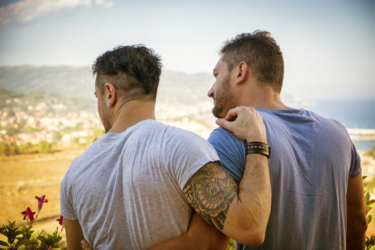 Back view of homosexual couple embracing nd looking at each other on background of resort.