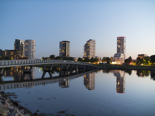 Obraz na płótnie Canvas Bridge over shallow water and large buildings forming Amager city skyline in the evening while reflecting in the water