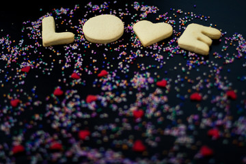 Love word made with homemade cookies in black table and colors sparks
