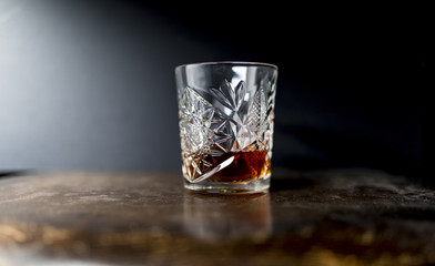 Whiskey (or whisky) in a luxury heavy cut crystal glass tumbler on a wooden table against a dark background