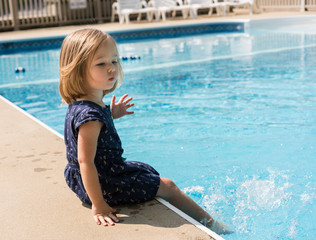Naklejka premium Small girl kicking the water in a swimming pool