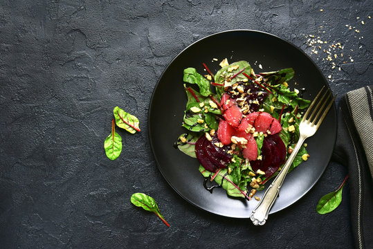Delicious sald with chard leaves, beetroot and grapefruit slices on a black plate over dark slate or stone background.Top view.