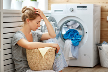 tired housewife woman in stress sleeps in laundry room with washing machine  .