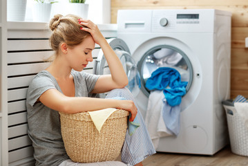 tired housewife woman in stress sleeps in laundry room with washing machine  .