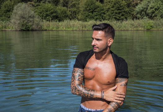 Young handsome tattooed man in wet clothes in the pond.