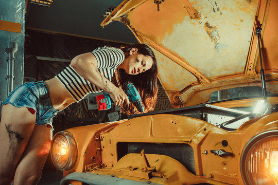 Young sexy woman mechanic is fixing engine at the repair garage