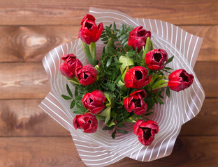 Bouquet of red tulips in a package of paper on wooden background Flat lay