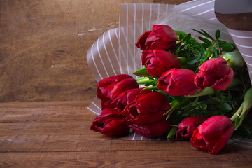 Bouquet of red tulips in a package of paper on wooden background