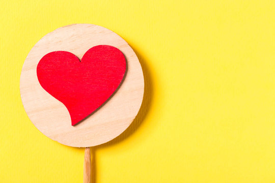 Valentine day concept. Red decorative heart with a stick on yellow background. Free space for your text.