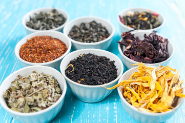 herbs and teas in bowls to make tea on blue table background cl