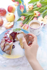 A bouquet of fresh tulips. Sweet home cupcake with sugar. Coffee in a cup. Apples on the table. The hand holds the cupcake.