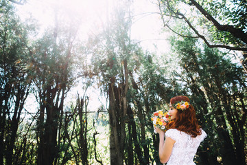 Portrait of a beautiful red-haired bride with flowers in her hair. She sniffs a wedding bouquet