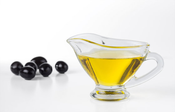 Olive oil in a gravy boat and black olives isolated on white background. Selective focus.