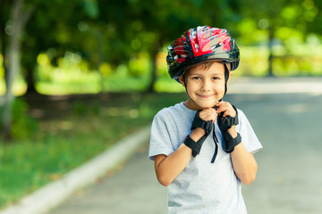 Little boy riding on rollers in the summer in the Park. Happy child in helmet learning to skate. Safety in sport.