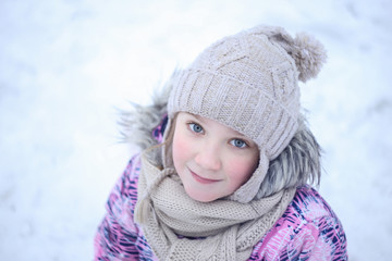 beautiful little girl with blue eyes in winter sportswear .winter snow background, looking at camera and smiling.