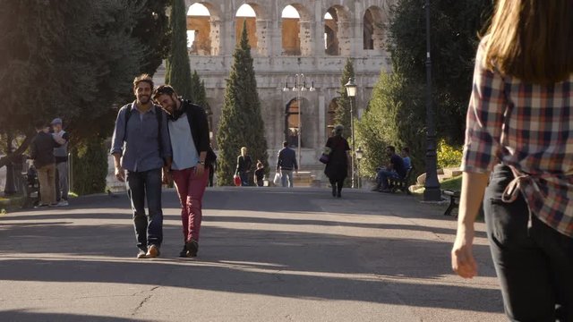 Young happy gay couple tourists walk in park road with trees colosseum in background in rome at sunset holding hands lovely slow motion colle oppio