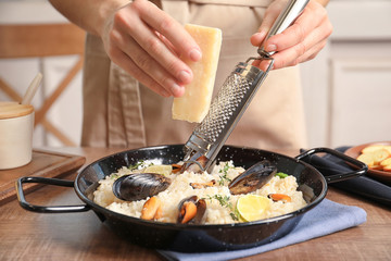 Young woman grating cheese on delicious seafood risotto at wooden table
