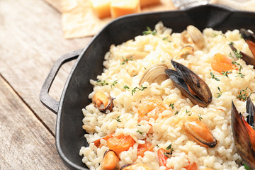 Frying pan with delicious seafood risotto on wooden table