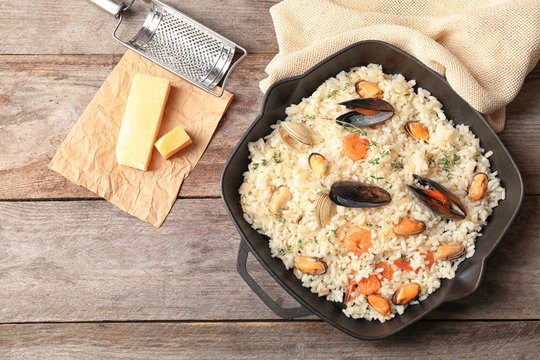 Frying pan with delicious seafood risotto on wooden table