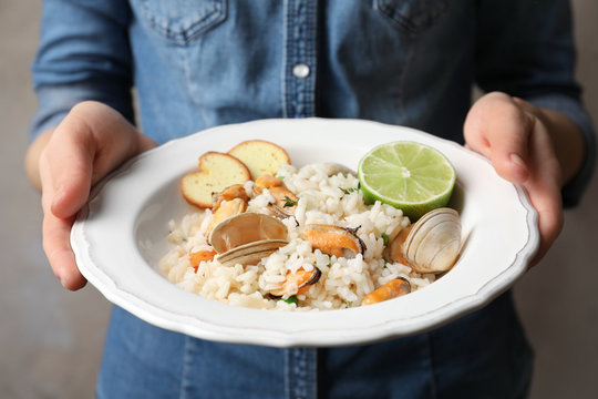 Young woman holding plate with delicious seafood risotto on blurred background